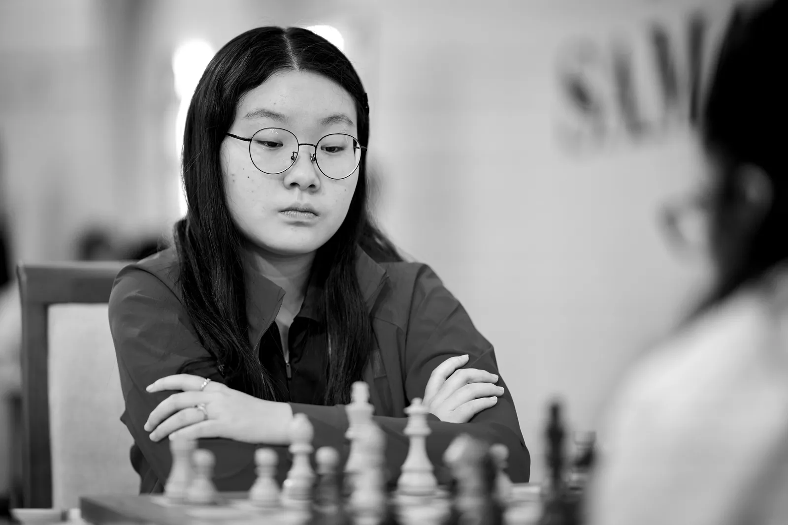 Lu Miaoyi, arms folded, looks down at the board.