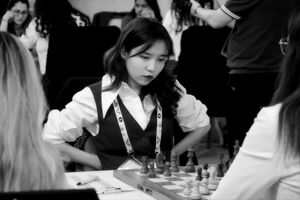 Alua Nurman, in a white blouse and dark waistcoat, studies the position at the board.
